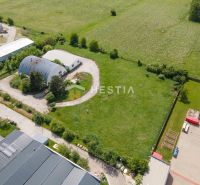 Skladový areál s pozemkom 10 000 m2 v priemyselnej zóne - Letecký pohľad na sklady a haly v Senici obklopené zeleňou a poľami.