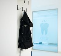 Kompletne zariadená zubná ambulancia, Záhorská Bystrica - Čierna bunda visiaca na vešiaku, v pozadí logo kliniky, na ulici Kunovská.