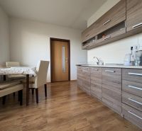 Na predaj: Veľký 2 izb.byt + LOGGIA + ŠPAJZA + PIVNICA - Kuchyňa v 2-izbovom byte s linkou, stolom a podlahou s dreveným dekorom.