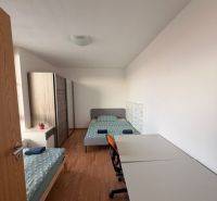 4-izbový byt, Bratislava/Nové Mesto, ulica Nová Rožňavská - Izba so stolom, dvoma posteľami a podlahou s dreveným dekorom v 4-izbovom byte.