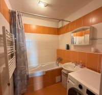 4-izbový byt, Bratislava/Nové Mesto, ulica Nová Rožňavská - Kúpeľňa so sprchovým závesom, práčkou a oranžovými obkladmi v 4-izbovom byte.