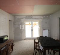 Na predaj - Dom s veľkým pozemkom v Pakostove - Nedokončený interiér s kuchynským stolom, stoličkami a skriňou v rodinnom dome.