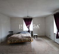 Na predaj - Dom s veľkým pozemkom v Pakostove - Izba s posteľou, stoličkou a stolíkom, podlaha s dreveným dekorom, závesy na oknách.