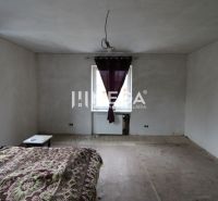 Na predaj - Dom s veľkým pozemkom v Pakostove - Spálňa v rodinnom dome s odlupujúcou sa podlahou a fialovými závesmi.