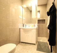 NA PRENÁJOM: Kancelárske priestory + 3-izbový apartmán – Košice - Kúpeľňa s béžovými obkladmi, bielou skrinkou, zrkadlom, vešiakom a zeleným koberčekom.