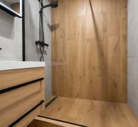 Kompletne zrekonštruovaný 2-izbový byt s 9 m² loggiou Sever - Kúpeľňa v 2-izbovom byte s podlahou s dreveným dekorom, sprchou a umývadlom.