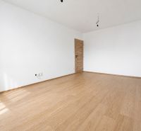 Kompletne zrekonštruovaný 2-izbový byt s 9 m² loggiou Sever - Prázdna izba s podlahou s dreveným dekorom a bielymi stenami v 2-izbovom byte.