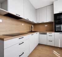 Kompletne zrekonštruovaný 2-izbový byt s 9 m² loggiou Sever - Kuchyňa v 2-izbovom byte s bielymi skrinkami a podlahou s dreveným dekorom.