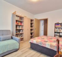 PRIESTRANNÝ BYT NA KARPATSKEJ ULICI, 80M2, SÁSOVÁ - Izba v 3-izbovom byte s podlahou s dreveným dekorom, knihovnicami a pohovkou.