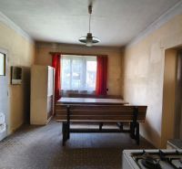 Znížená cena!!! Vidiecky dom v obci Olováry v okrese Veľký Krtíš. - Kuchyňa v rodinnom dome s jedálenským stolom, sporákom a červenými záclonami.