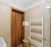 1-IZBOVÝ BYT S VEĽKOU 12 m² TERASOU | SLNEČNICE VILADOMY - Kúpeľňa v 1-izbovom byte s drevenými dverami, sprchovým kútom a radiátorom.