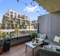 1-IZBOVÝ BYT S VEĽKOU 12 m² TERASOU | SLNEČNICE VILADOMY - Balkón s pohodlným sedením a výhľadom na moderné budovy na Fialovej v Bratislave V.