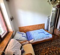 3-IZBOVÝ BYT 90 m² V RODINNOM DOME | POVAŽSKÝ CHLMEC - Žilina - Izba v rodinnom dome so starým kobercom, kreslom a posteľou pri okne.