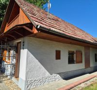 Víkendová chalupa Mikušovce, pozemok 281m2 - Rodinný dom v Mikušovciach s drevenými okenicami a červenou strechou obklopený zeleňou.