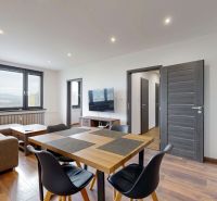 BENADOVA - 4-IZBOVÝ BYT PO KOMPLETNEJ REKONŠTRUKCII, 79 m², LOGGIA  - Obývačka v 4-izbovom byte s pohovkou, jedálenským stolom a podlahou s dreveným dekorom.