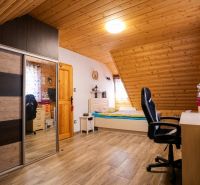 NOVOSTAVBA DOMU V MODERNOM VIDIECKOM ŠTÝLE, OBKLOPENÁ PRÍRODOU A S VEĽ - Podkrovná izba s dreveným obkladom stropu, posteľou, skriňou a podlahou s dreveným dekorom.