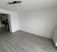 3-IZBOVÝ TEHLOVÝ BYT V DUBNICI N/V, BALKÓN, VLASTNÉ KÚRENIE A VÝBORNÉ  - Obývacia izba 3-izbového bytu s podlahou s dreveným dekorom a kuchyňou na ľavej strane.