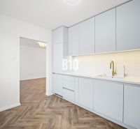 Prémiové bývanie v centre Nitry | 3 izby, veľký balkón - Kuchyňa v 3-izbovom byte s bielym nábytkom a podlahou s dreveným dekorom.