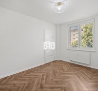 Prémiové bývanie v centre Nitry | 3 izby, veľký balkón - Izba v 3-izbovom byte s podlahou s dreveným dekorom a veľkým oknom.