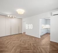Prémiové bývanie v centre Nitry | 3 izby, veľký balkón - Obývacia izba v 3-izbovom byte s podlahou s dreveným dekorom a vstavanou skriňou.