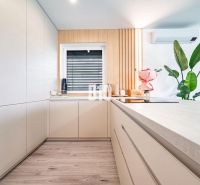 5 izb. bungalov s bazénom, garáž, RED OAK - Nitra, Lužianky - Kuchyňa v rodinnom dome s podlahou s dreveným dekorom, bielymi skrinkami a kvetmi.
