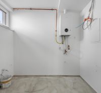 Moderný rodinný dom, ktorý vás prekvapí priestorom aj atmosférou - Biela miestnosť s bojlerom a podlahou s dreveným dekorom v rodinnom dome.