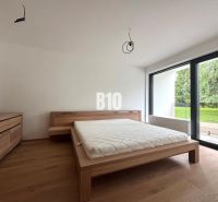 Relax Residence - Apartmán so zariadením - Spálňa s posteľou a komodou, podlaha s dreveným dekorom, veľké okno smerujúce do záhrady.