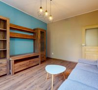 Priestranný 2i byt v obklopení zelene len pár krokov od OC Nivy | 53m² - Obývačka s modrou stenou, dreveným nábytkom a podlahou s dreveným dekorom.