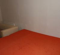 Dvojizbový byt v rodinnom dome v Seredi na prenájom  - Izba s oranžovou posteľou a beige kreslom v 2-izbovom byte.