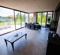 Na predaj 5i rodinný dom, novostavba, Vráble, pozemok 1200m2 - Presklená terasa rodinného domu s výhľadom na záhradu a dlažbovou podlahou.