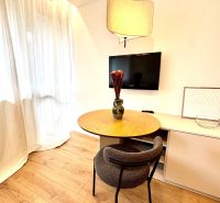 Na predaj úplne nový 1i byt od architekta v tichej časti Dúbravky - Stôl so stoličkou a televízorom v 1-izbovom byte, podlaha s dreveným dekorom.