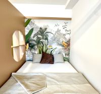 Na predaj úplne nový 1i byt od architekta v tichej časti Dúbravky - Posteľ so vzorovanou dekou, v 1-izbovom byte s tropickou tapetou a vankúšmi.