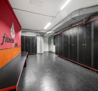 Na predaj PRIESTRANNÉ FITNESS CENTRUM na LUKRATÍVNEJ ADRESE RUŽINOVA - Fitness šatňa s čiernymi skrinkami a červenou stenou v obchodných priestoroch.