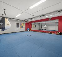 Na predaj PRIESTRANNÉ FITNESS CENTRUM na LUKRATÍVNEJ ADRESE RUŽINOVA - Tréningová miestnosť s vrecom, zrkadlami a modrou žinenkou na podlahe s dreveným dekorom.