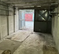 18 m2 Garáž na Sliačskej ulici v Bratislave - Betónová garáž s otvorenými oceľovými dverami, pohľad na ďalšiu garáž vonku.