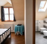 I Radový 4- izb. rodinný dom v starej časti Rače na Alstrovej - Podkrovná izba s oknom, posteľou, kúpeľňou a podlahou s dreveným dekorom v rodinnom dome.