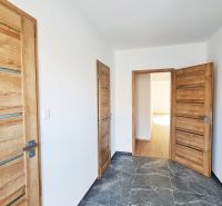 / Novostavba, moderný bungalov, dokončený na kľúč  - Chodba v rodinnom dome s dlažbou a drevenými dverami, biele steny.