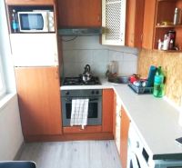 1- izbový byt - Košice - Juh, Ostravská ulica - Kuchyňa v 1-izbovom byte s podlahou s dreveným dekorom, základnými spotrebičmi a skrinkami.