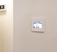 MINÚTU OD NÁMESTIA - VEĽKÁ GARSÓNKA V CENTRE - Nastaviteľný termostat na stene v garsónke, jednoduchý dizajn, biele pozadie.