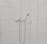 NOVÁ GARSÓNKA V CENTRE - MINÚTU OD NÁMESTIA - Sprchový kút s bielymi obkladačkami a sprchovou hlavicou v garsónke.