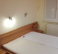 Na prenájom 3-izbový byt so záhradkou v Nových Zámkoch - Spálňa 3-izbového bytu s drevenou posteľou a oknom s roletami na stene.