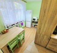 4 izbový byt Bánovce nad Bebravou /CENTRUM - STRED / 80 m2/ PIVNICA - Kuchyňa v 4-izbovom byte so stolom, zelenými stoličkami a podlahou s dreveným dekorom.