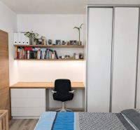 MODERNÁ ZARIADENÁ NOVOSTAVBA  takmer v centre - MAHULANKA - Spálňa v 2-izbovom byte s pracovným kútom, knihami a podlahou s dreveným dekorom.
