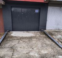 Garáž Púpavova, Karlova Ves + pivnica - Sivá garáž na ulici Púpavová, obklopená stromami, príjazdová cesta pred garážou.