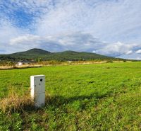 Stavebný pozemok 673 m2 v Štitároch s výhľadom na Zobor i Žibricu - Zelená lúka s domami a kopcom v pozadí v Štitároch, Pozemky - bývanie.