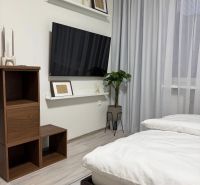 Garzónka Záhradnícka ul.,Staré Mesto,so zariadením,parkovanie vo dvore - Spálňa garsónky s televízorom na stene, bielymi závesmi a dreveným nábytkom.