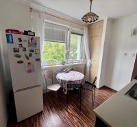 2 izbový byt na prenájom s balkónom na Kalinčiakovej, voľný od 01.10.2 - Kuchyňa v 2-izbovom byte s podlahou s dreveným dekorom, jedálenským stolom a chladničkou.
