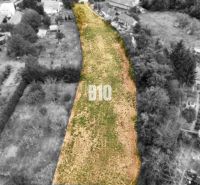 Na predaj pozemok v Kolíňanoch – 2 700 m² - Pozemky - bývanie Kolíňany: Dlhý pozemok so zelenou trávou, lemovaný stromami a stavbami.
