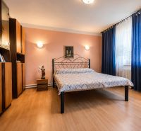 Na predaj zrekonštruovaný 4-izbový rodinný dom v Šalgočke  - Spálňa s kovovou posteľou, podlaha s dreveným dekorom, nábytok a závesy v rodinnom dome.