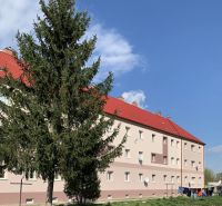Krásny 1 izbový byt  45m2 + garáž - Budova s červenými strechami a pred ňou strom, na Železničnej ulici v Šahách.